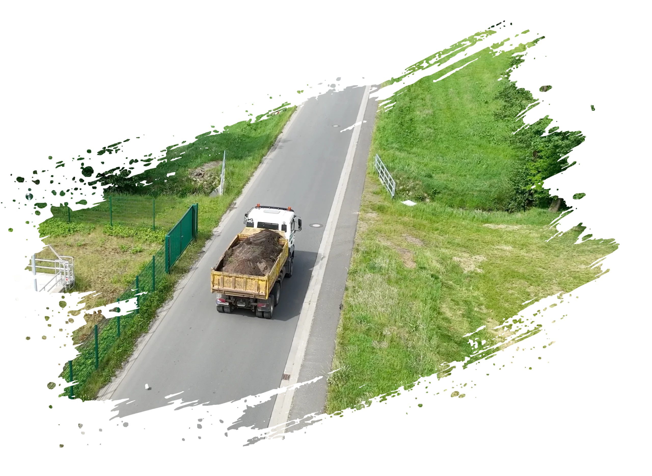 Luftaufnahme eines Lastwagens mit gelbem Kipper auf schmaler Straße, umgeben von grüner Landschaft.